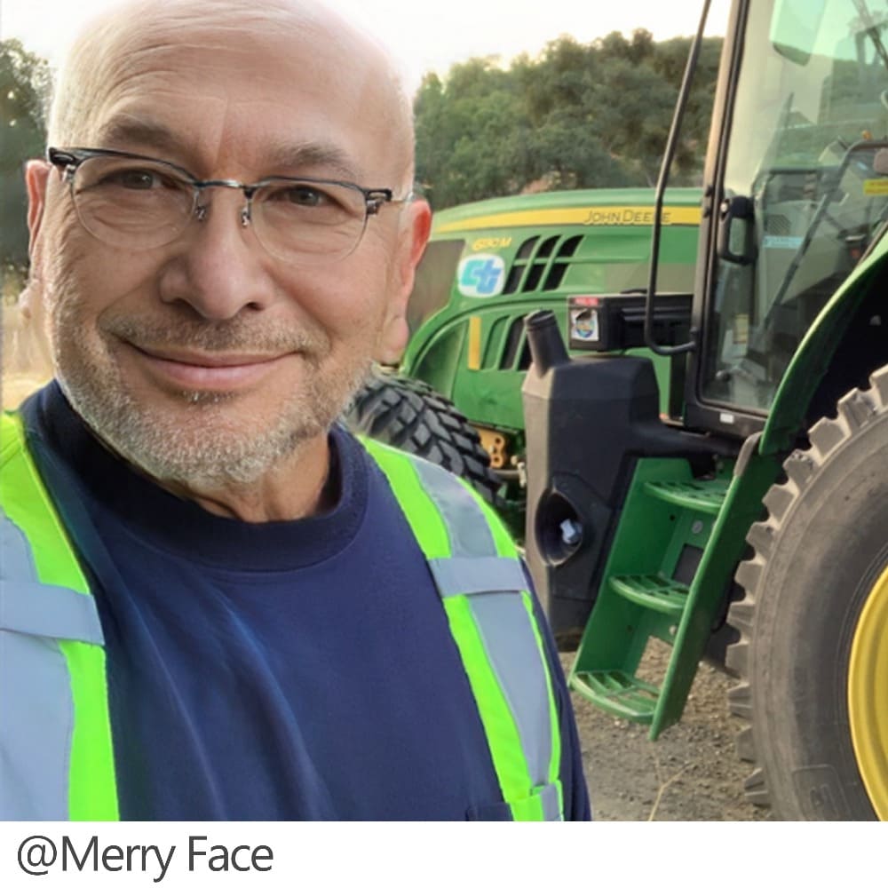 Man wearing glasses and a safety vest standing next to a tractor.